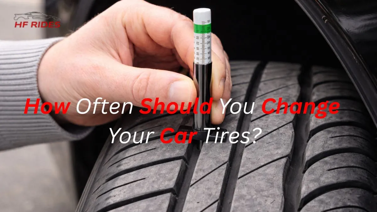 A hand holding a tread depth gauge measures a car tire's tread, indicating safety checks. The tire appears worn, highlighting maintenance importance. - How often should you change your tires